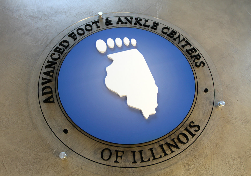 36" Diameter Circle Frosted Acrylic Panel Sign with Raised Black Lettering and Blue inner circle IL foot shape will be additional raised white acrylic piece on top all assembled flush on face installed with (3) standoffs for interior lobby drywall