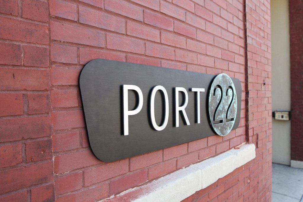 53'' overall width 3/8'' thick brushed aluminum back plate anodized black (black shape) with 1/4'' thick brushed stainless steel letters (PORT) and 1/4'' thick verde painted speckle (circle 22) assembled on face with spacers. Blind studs for brick on bac